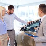 happy couple with car dealer in auto show or salon